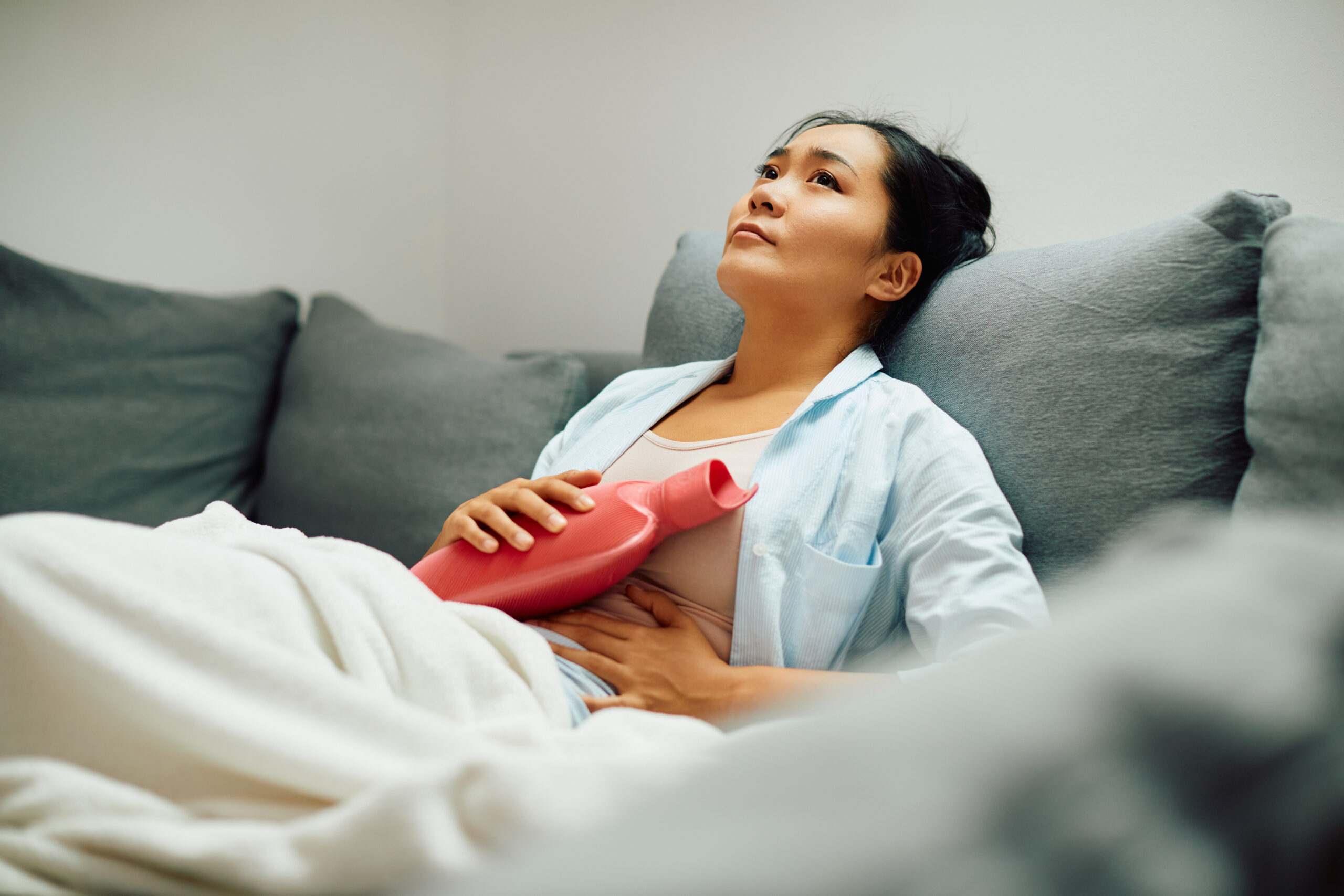 Femme allongée sur un canapé avec une bouillotte sur le ventre pour soulager une douleur liée à l'endométriose